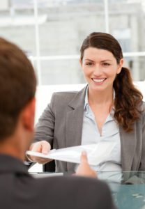 A woman is smiling while holding papers in her hand.